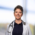 Dr. Jill Crista wearing a white coat with a stethoscope around her neck against a blurred background