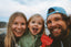 Family of three outdoors with a red object, smiling at the camera.