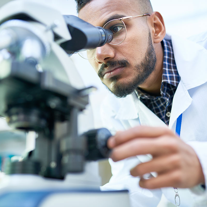 Portrait of young Middle-Eastern scientist looking in microscope while working on medical research in science laboratory.